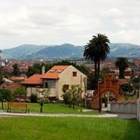 Cabaña con techo de terracota, palmeras y entrada arqueada con vista a un paisaje urbano y montañas distantes.
