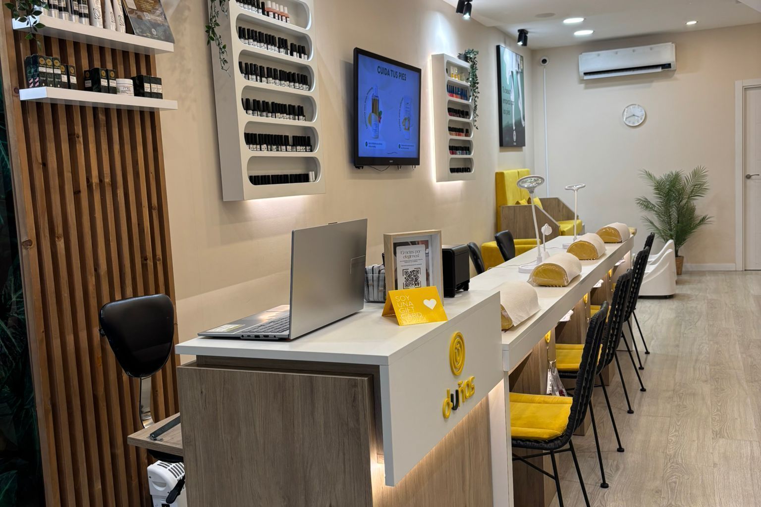 El interior de un salón de manicura moderno, con un mostrador de madera clara, expositores de esmaltes de uñas