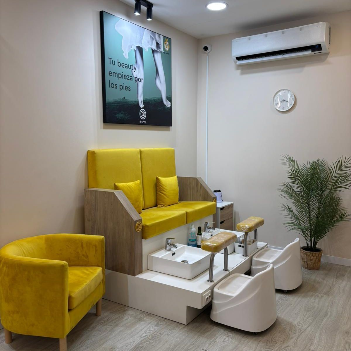 Un luminoso puesto de pedicura con dos sillas amarillas, lavabos para los pies, un aparato de aire acondicionado de pared