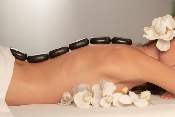 Piedras de masaje de spa en la espalda de una persona con flores de orquídea blanca cerca.