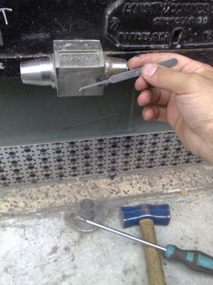 Una mano sostiene una herramienta junto a un martillo y un destornillador.