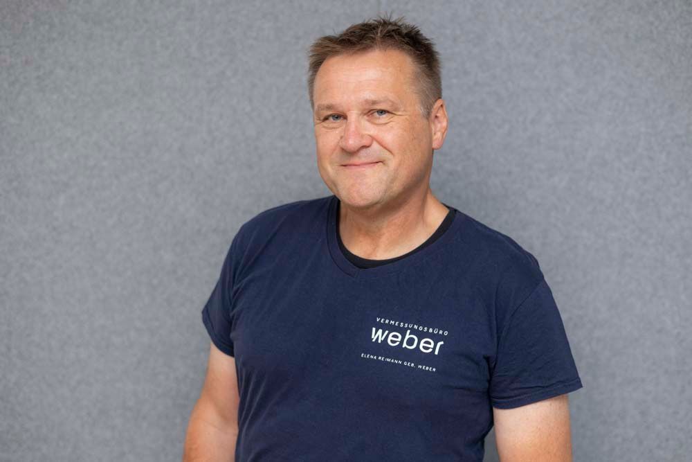 Ein Mann in einem karierten Hemd lächelt in die Kamera , während er auf einem Stuhl sitzt.