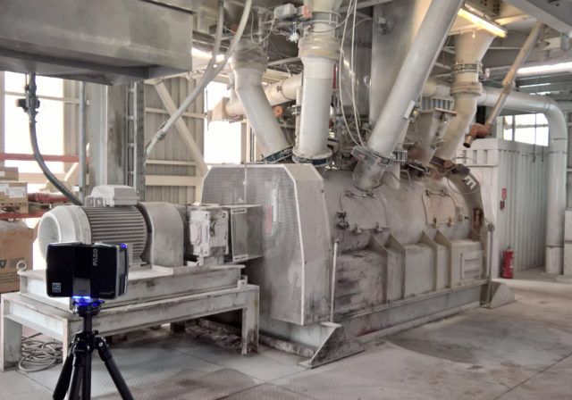 Eine große Industriemaschine in einer Fabrikumgebung, mit einem Gerät auf einem Stativ im Vordergrund.