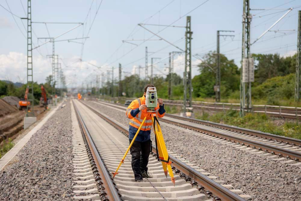 Vermesser in Sicherheitsweste verwendet eine Totalstation auf Bahngleisen, um die Ausrichtung einer Eisenbahnstrecke zu messen.