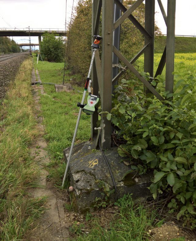 Ein Vermessungsinstrument, das in der Nähe einer Eisenbahnstrecke und eines Strommasts aufgestellt ist.