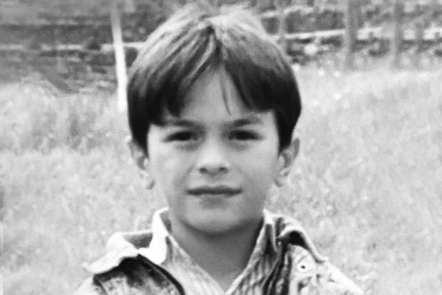 Ein Schwarzweißfoto eines kleinen Jungen, der im Gras steht.