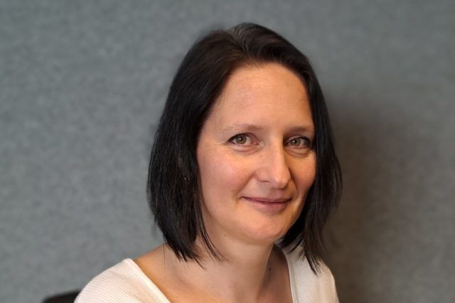 Eine Frau mit dunklem Haar lächelt und trägt ein weißes Hemd