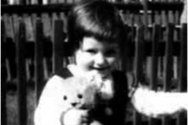 Auf einem Schwarzweißfoto hält ein kleines Mädchen einen Teddybären.