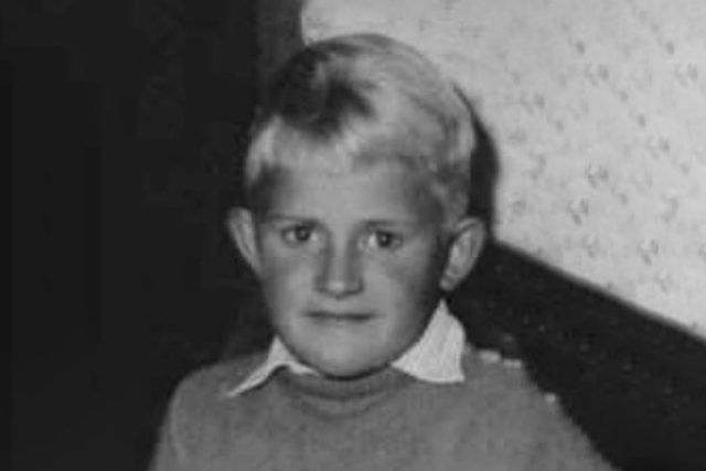 Ein Schwarzweißfoto eines kleinen Jungen in Pullover und weißem Hemd.
