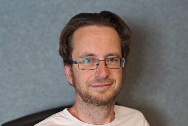 Ein Mann mit Brille und weißem Hemd lächelt in die Kamera.
