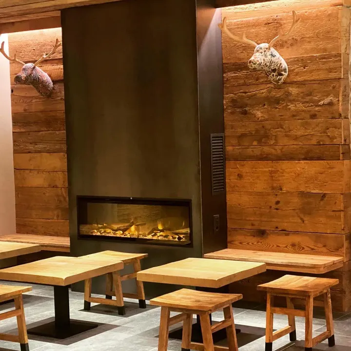 Acogedor salón moderno con chimenea, paredes de madera y mesas y taburetes pequeños.