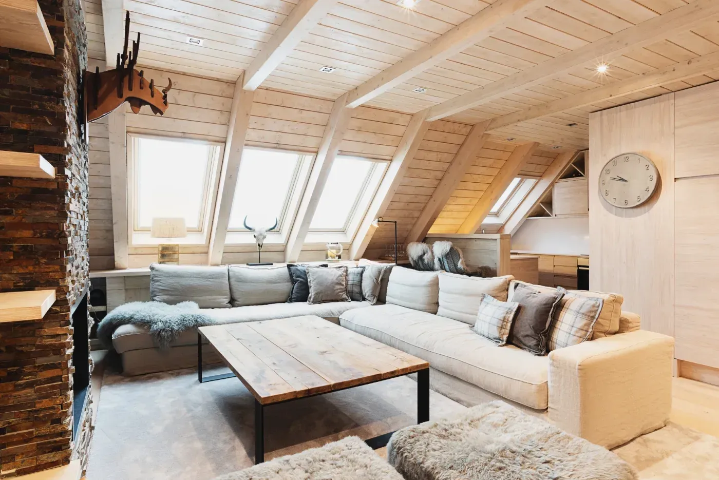 Acogedora sala de estar abuhardillada con tragaluces, sofá seccional gris y detalles rústicos de madera.
