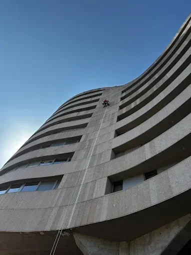 Fachada curva de un rascacielos fotografiada desde abajo contra un cielo azul.