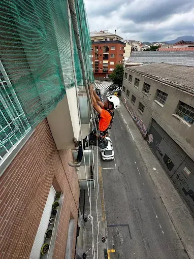 Obrero en un andamio de gran altura junto a un edificio de ladrillo, con la calle de la ciudad y coches aparcados debajo.