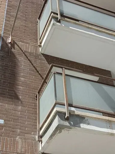 Balcones de apartamentos de ladrillo vistos desde abajo, con barandillas de cristal y una tubería de desagüe 