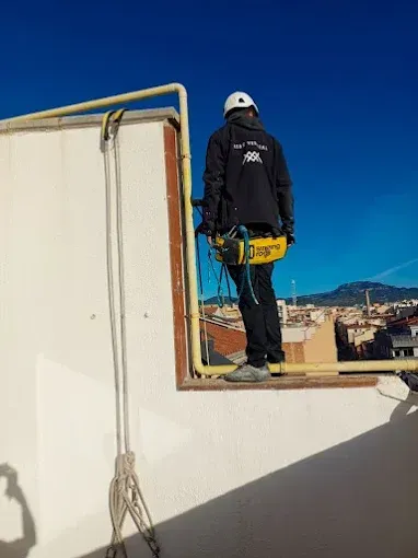 Un trabajador con equipo de seguridad se encuentra de pie en el borde de una azotea, utilizando un arnés