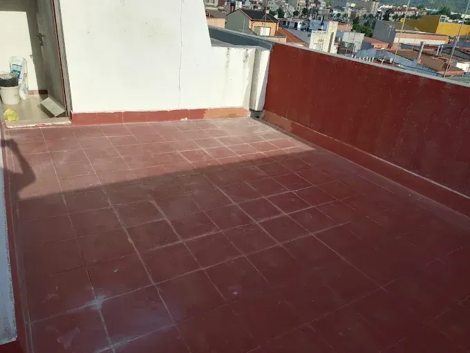 Terraza en la azotea con tejas rojas, un muro bajo blanco y edificios de la ciudad al fondo.