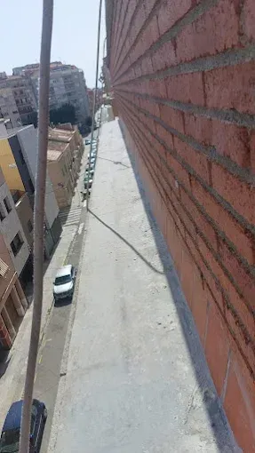 Estrecha pasarela en la azotea, junto a un muro de ladrillo rojo, con vistas a una calle de la ciudad con coches aparcados