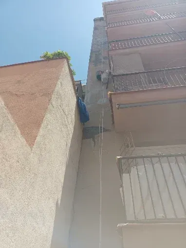 Un callejón estrecho entre edificios altos bajo un cielo azul brillante, con ropa tendida en un balcón.