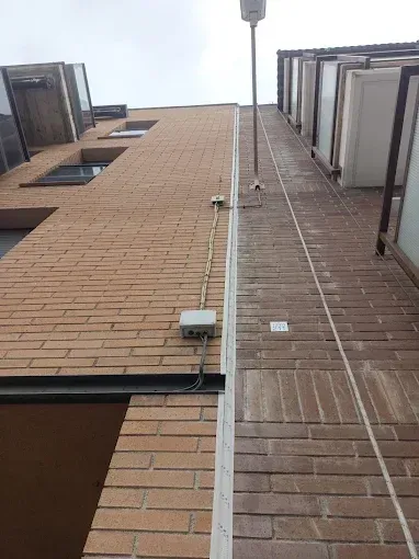 Vista desde abajo de dos paredes de ladrillo de un apartamento con ventanas y un bajante central, recortadas contra el cielo.