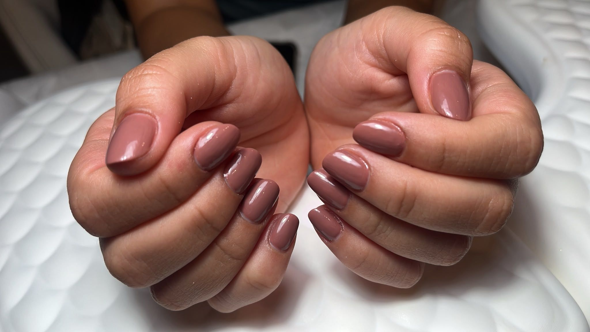 Manos con las uñas pintadas de color malva, unidas sobre una superficie blanca acolchada.