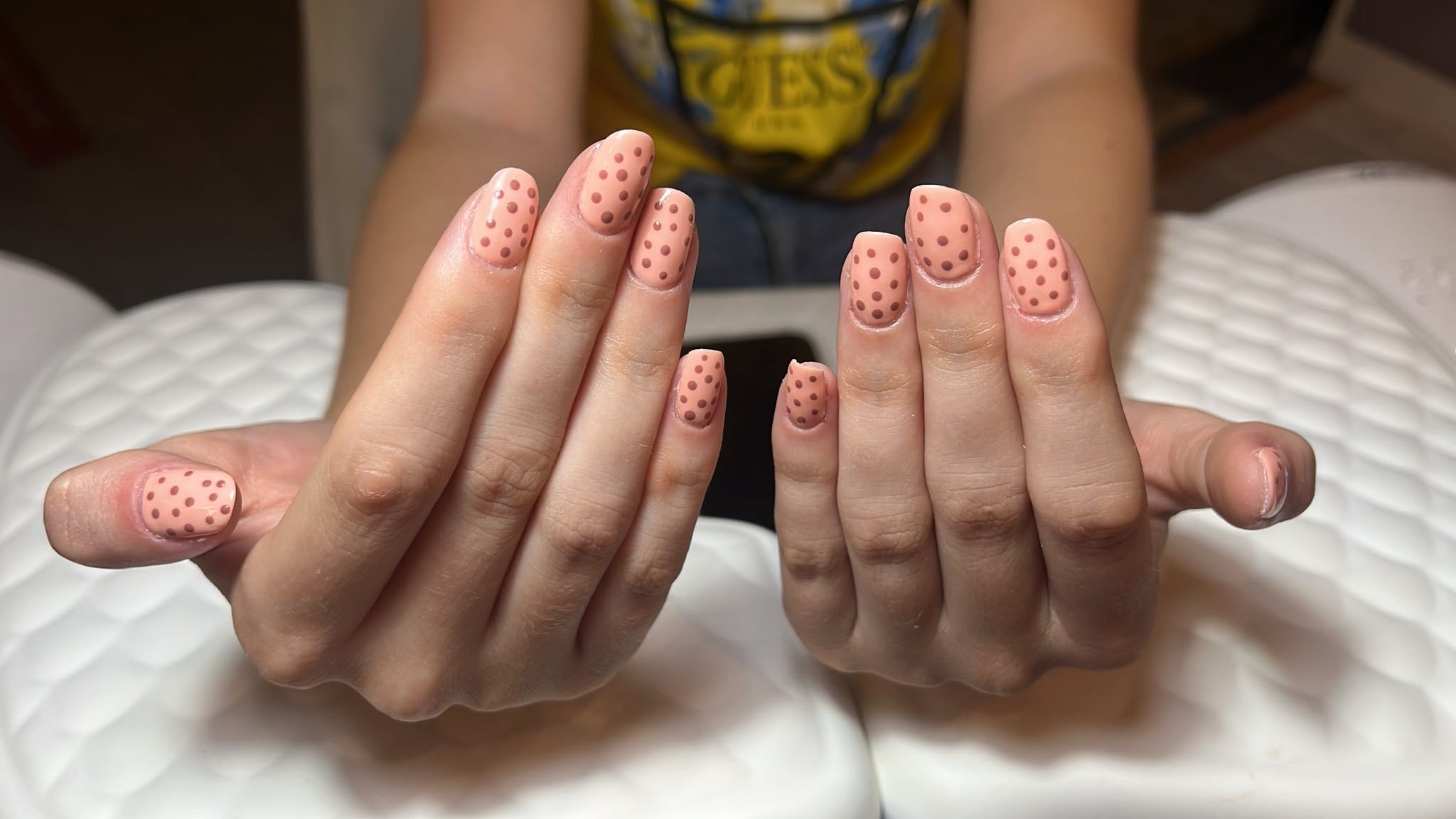 Dos manos con uñas decoradas con lunares de color coral, apoyadas sobre una manta blanca, con las palmas juntas.