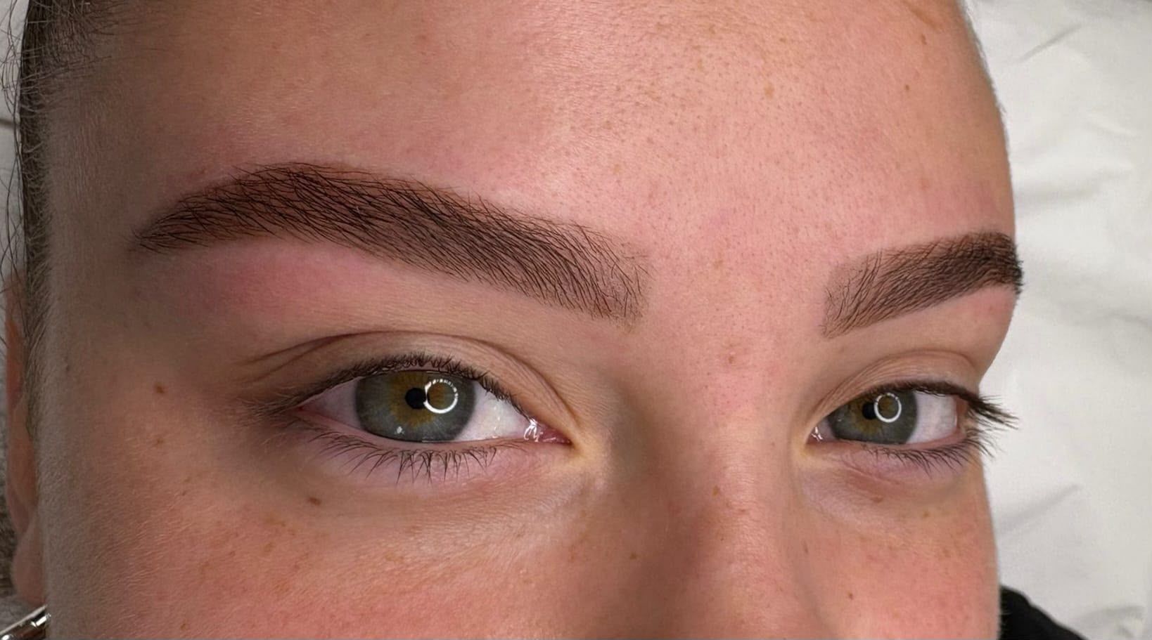 Primer plano de ojos y cejas con maquillaje de ojos verde y cejas definidas.