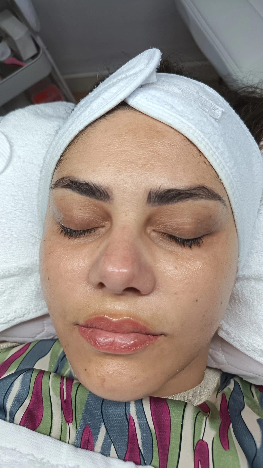 Una mujer envuelta en una toalla blanca y con una mascarilla facial descansa con los ojos cerrados