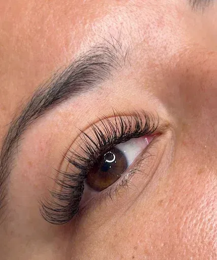 Primer plano de un ojo con extensiones de pestañas largas y rizadas y cejas bien definidas.