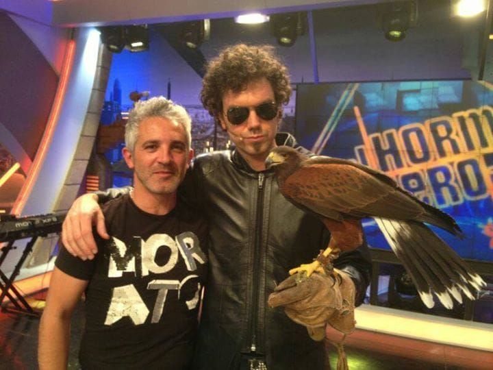 Dos hombres posan con un pájaro frente a un cartel que dice hormero