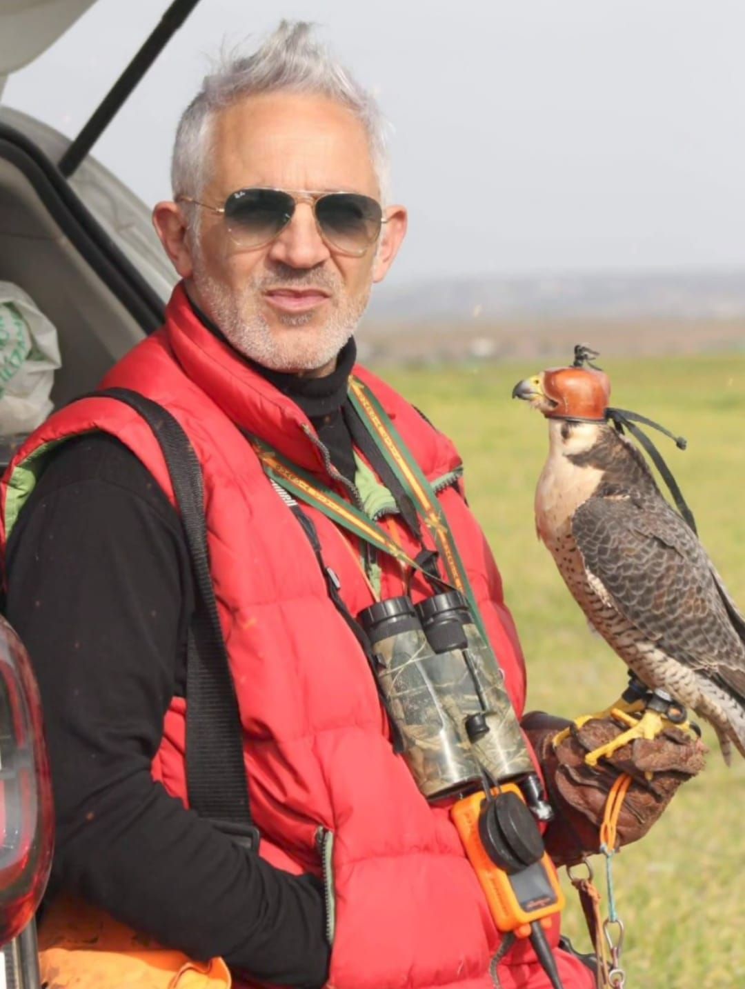 Un hombre con un chaleco rojo sostiene un pájaro en su mano.