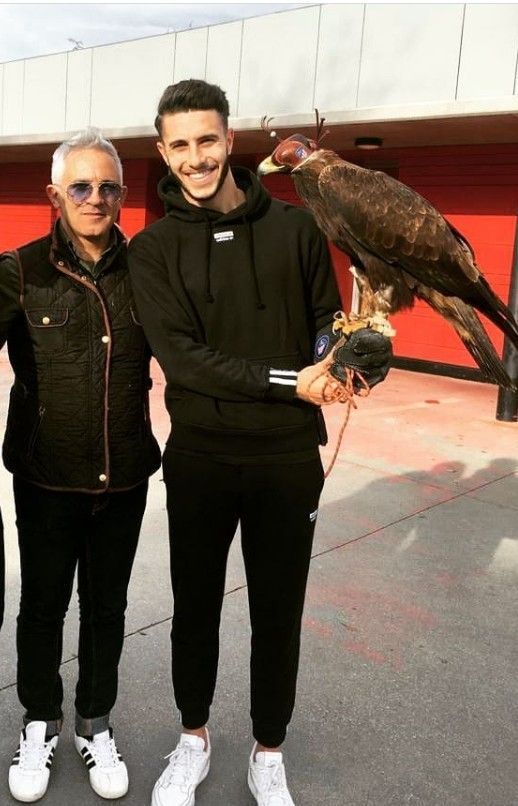 Dos hombres de pie uno al lado del otro sosteniendo un pájaro con una correa.
