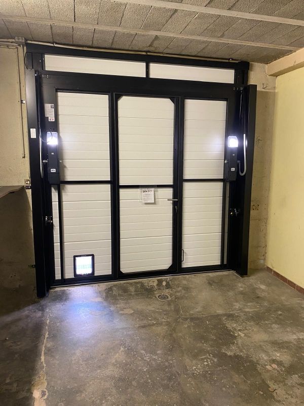 Porte de garage noire avec boutons lumineux dans une travée de garage en béton