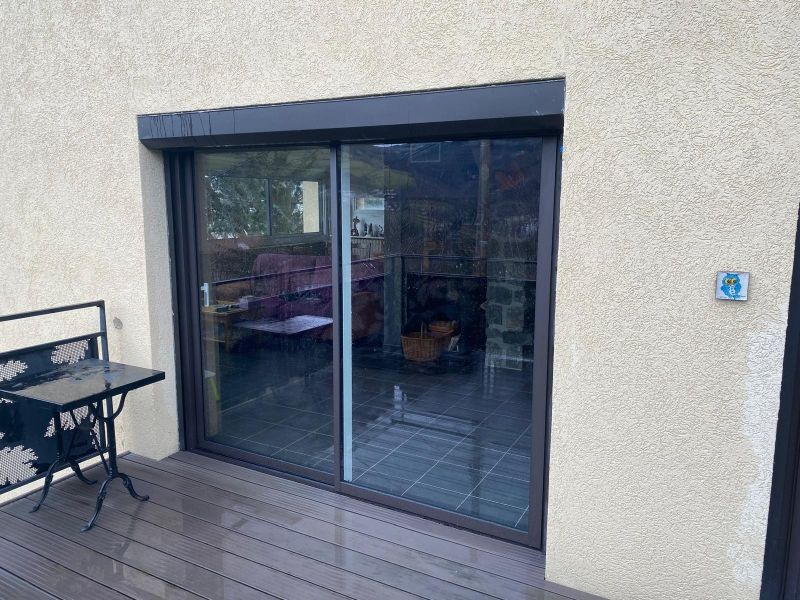 Porte-fenêtre coulissante sur un mur beige, donnant sur une terrasse en bois et une table d'extérieur.