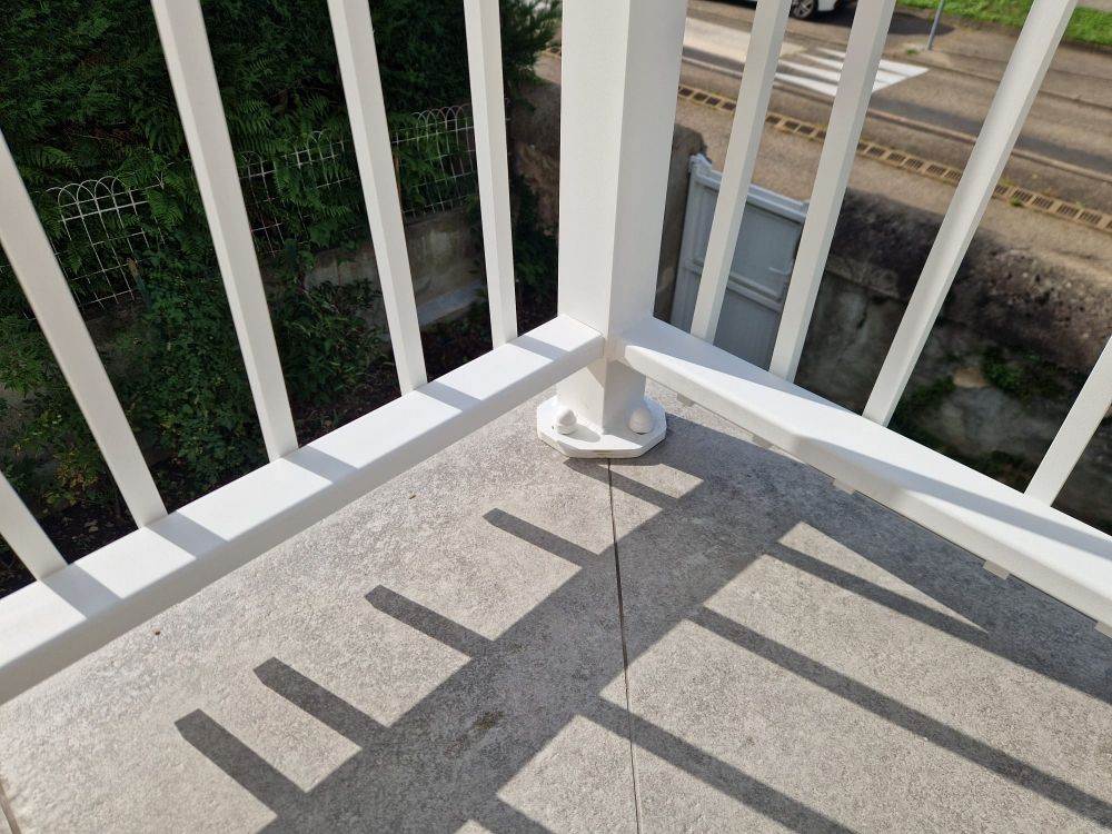 Un coin de rambarde blanche sur un balcon en béton projette des ombres sur la surface.