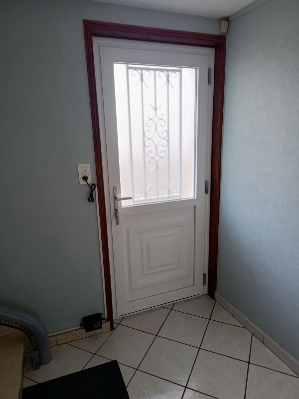 Porte blanche avec verre dépoli et barres métalliques décoratives, encadrée de bois, sur un sol carrelé.