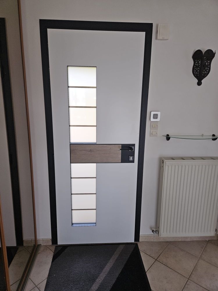Porte d'entrée blanche moderne avec panneaux en verre dépoli, moulures noires, radiateur mural et tapis de couloir à motifs