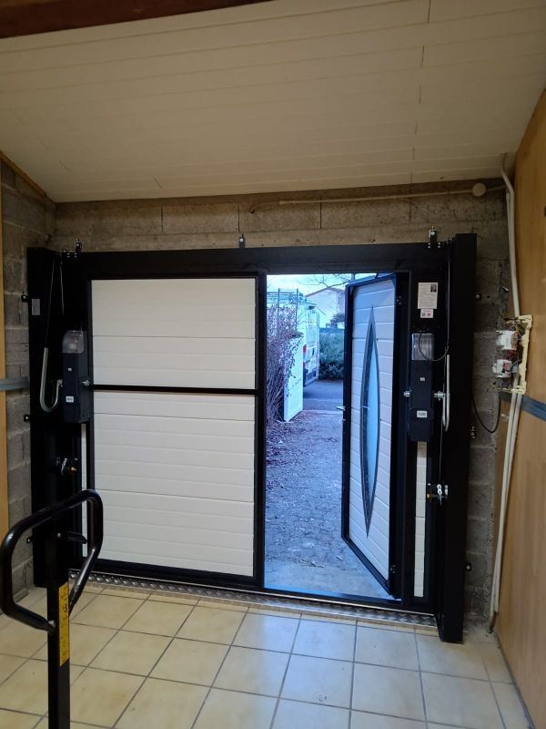Porte de garage ouverte avec un seuil surélevé et un sol carrelé intérieur donnant sur une cour extérieure.