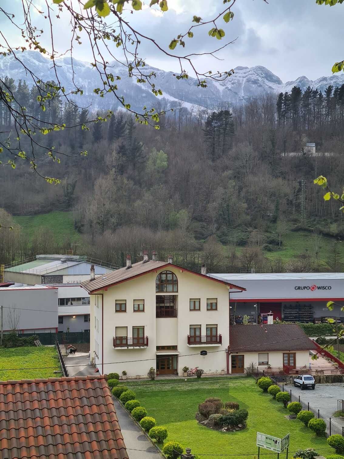Una casa con techo de tejas rojas está rodeada de árboles y montañas.