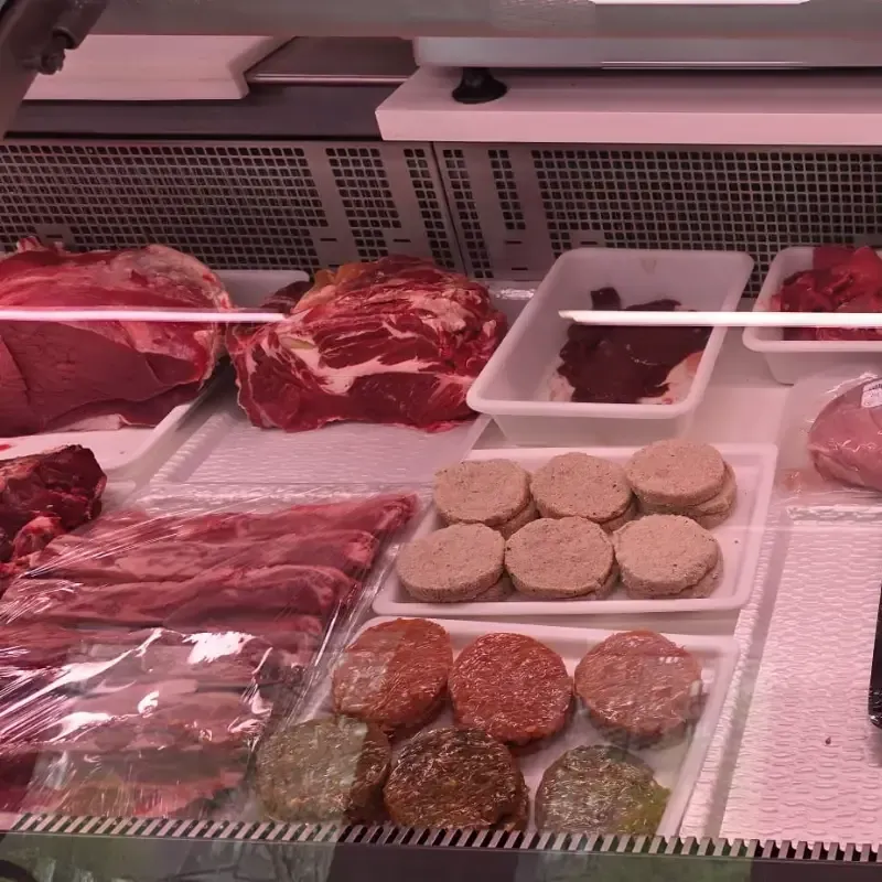 Una vitrina de carnicería que contiene varios cortes de carne cruda, incluyendo carne de res y varios tipos de hamburguesas.