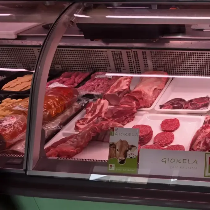 Una vitrina refrigerada de carnicería llena de diferentes cortes de carne cruda, hamburguesas y pequeños letreros.
