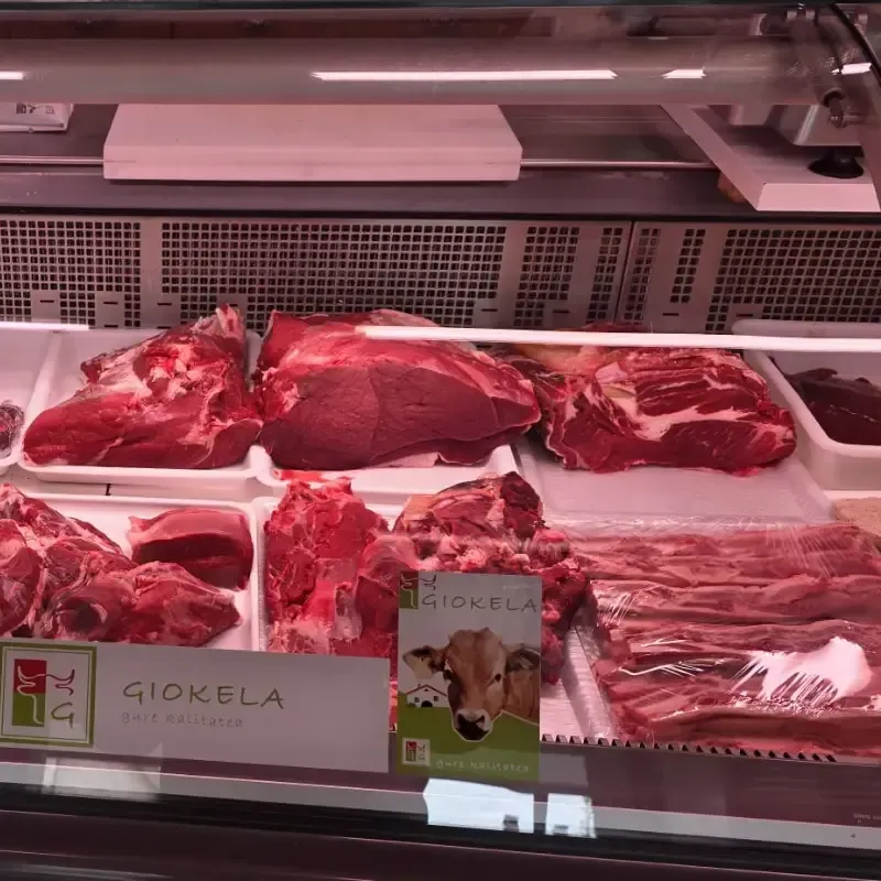 Una vitrina refrigerada de carnicería que contiene varios cortes de carne de res cruda, etiquetada como