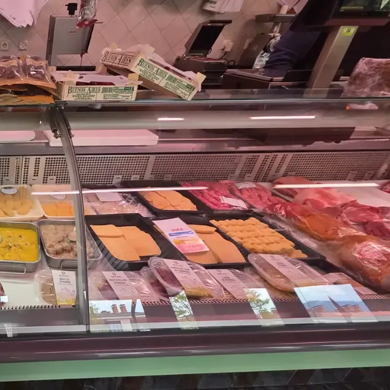 Una vitrina refrigerada de charcutería con varios tipos de carne y queso en una tienda.