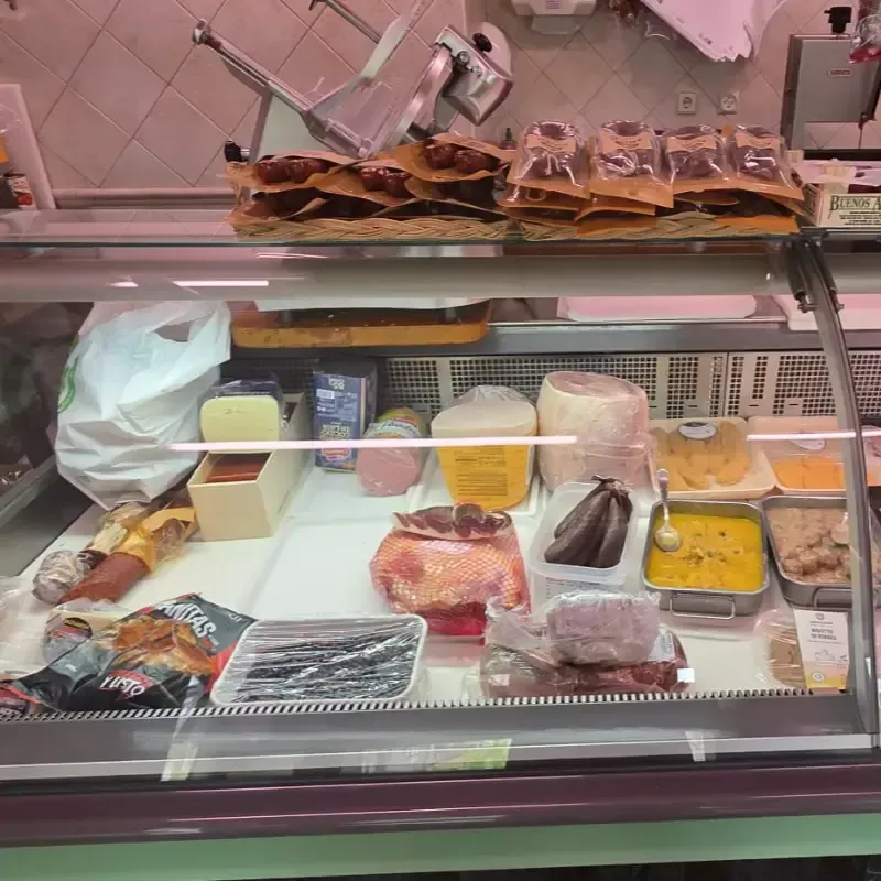 Una vitrina de charcutería repleta de diversos embutidos, quesos, aperitivos envasados y platos preparados.
