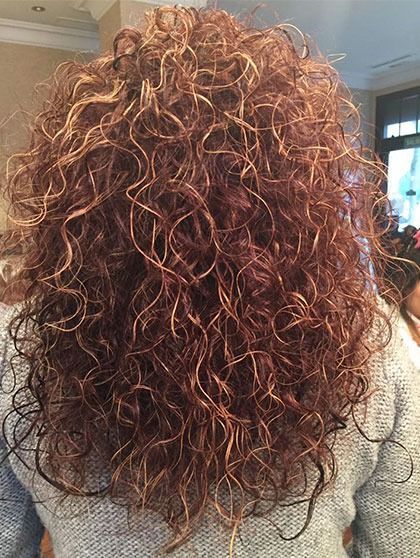 Una mujer con cabello rizado lleva un suéter gris.