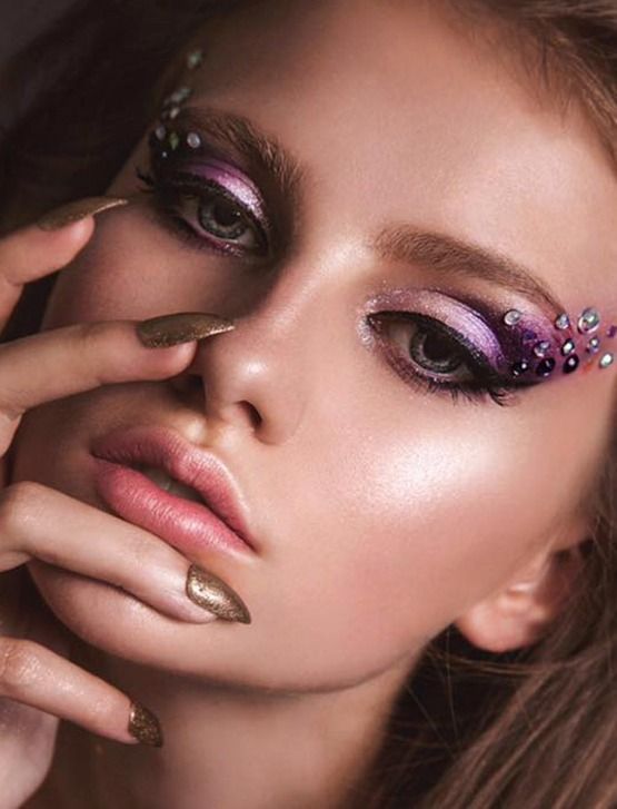 Un primer plano del rostro de una mujer con maquillaje de ojos morado y uñas doradas.