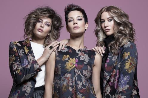 Tres mujeres están paradas una al lado de la otra sobre un fondo rosa.