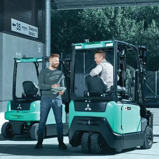 Dos hombres están parados junto a dos carretillas elevadoras en un estacionamiento.