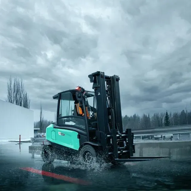 Una carretilla elevadora verde y negra circula bajo la lluvia.