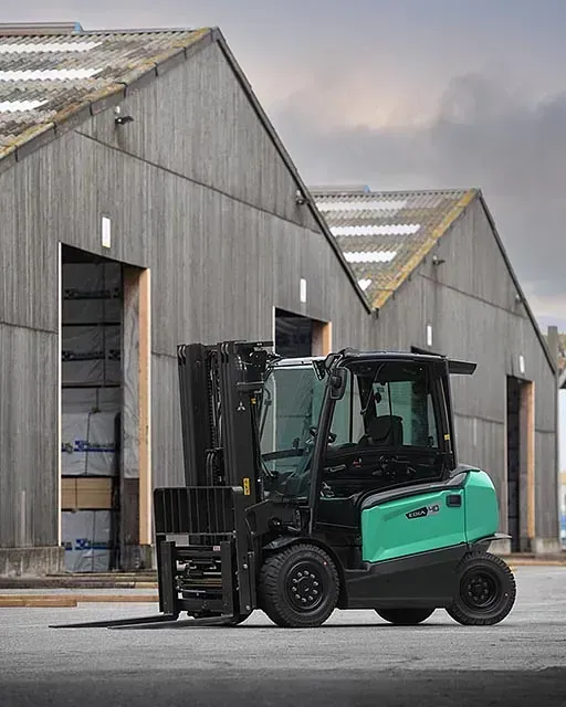 Una carretilla elevadora verde está estacionada frente a un almacén.